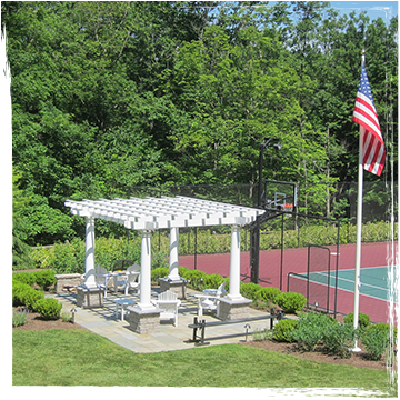 A white pergola and American flag beside an enclosed tennis court